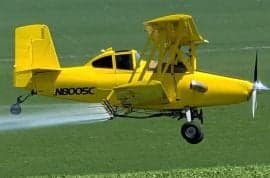 A yellow biplane crop duster sprays a field.