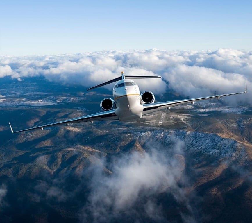 A Bombardier Global Express flying above mountains and clouds.