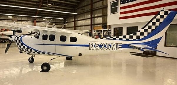 A Cessna 208 Caravan with a blue and checkerboard paint scheme, registration N535ME, parked in a hangar.