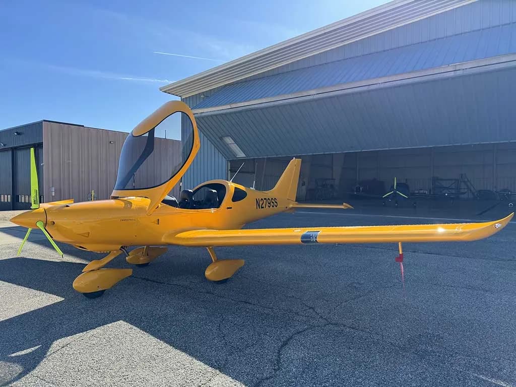 A yellow Bristell aircraft, N279SS, with its canopy open and a red pitot tube cover, is parked on the tarmac.