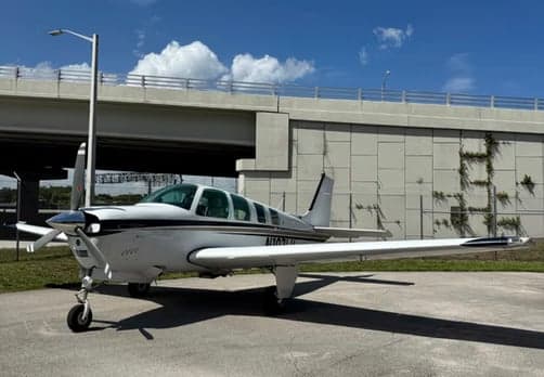 Another front-side view of the white single-engine aircraft N107LU with a black stripe, parked on a tarmac near a highway overpass.