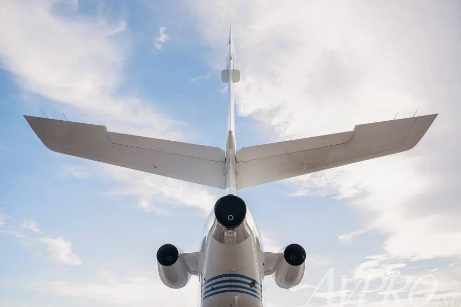 A rear view of the Dassault Falcon 900EX, N917JF, showing its distinctive T-tail and three engines against a cloudy sky.