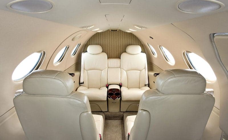 The interior of an aircraft cabin features cream-colored leather seats and wood trim.