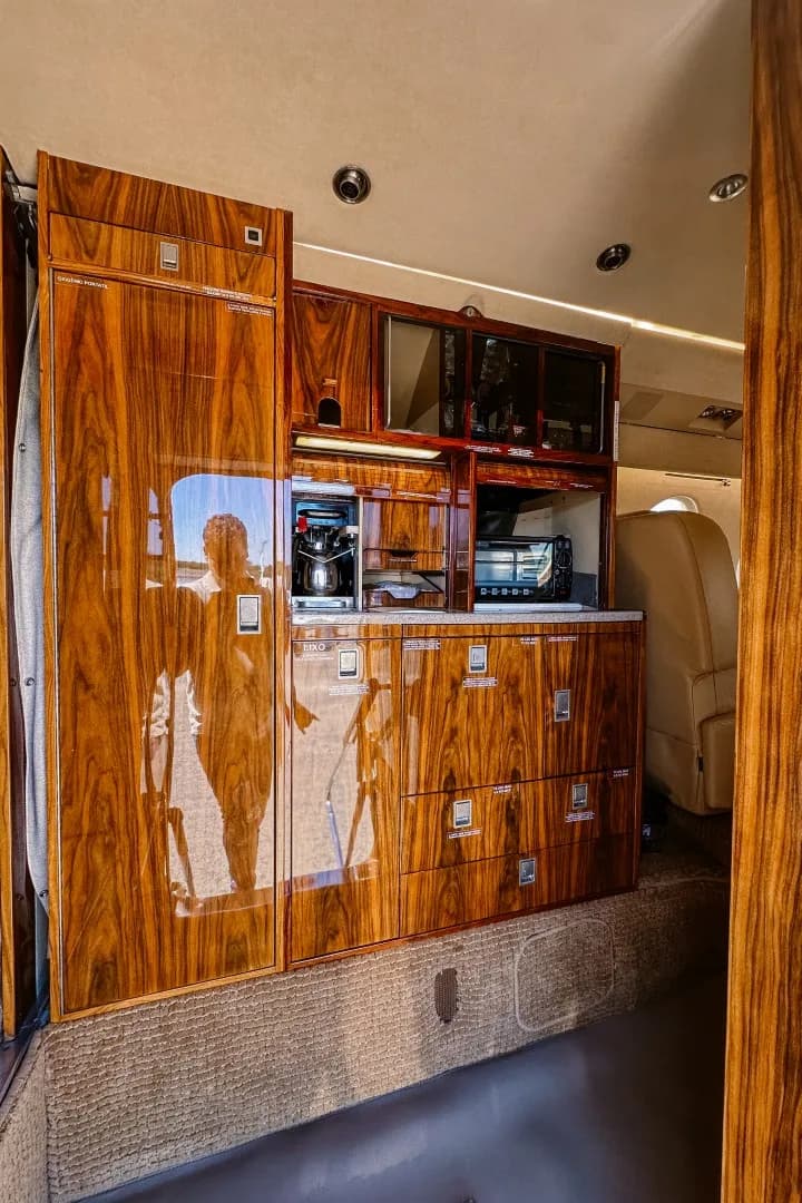 A well-appointed aircraft galley with dark polished wood cabinetry, a coffee maker, and a microwave.