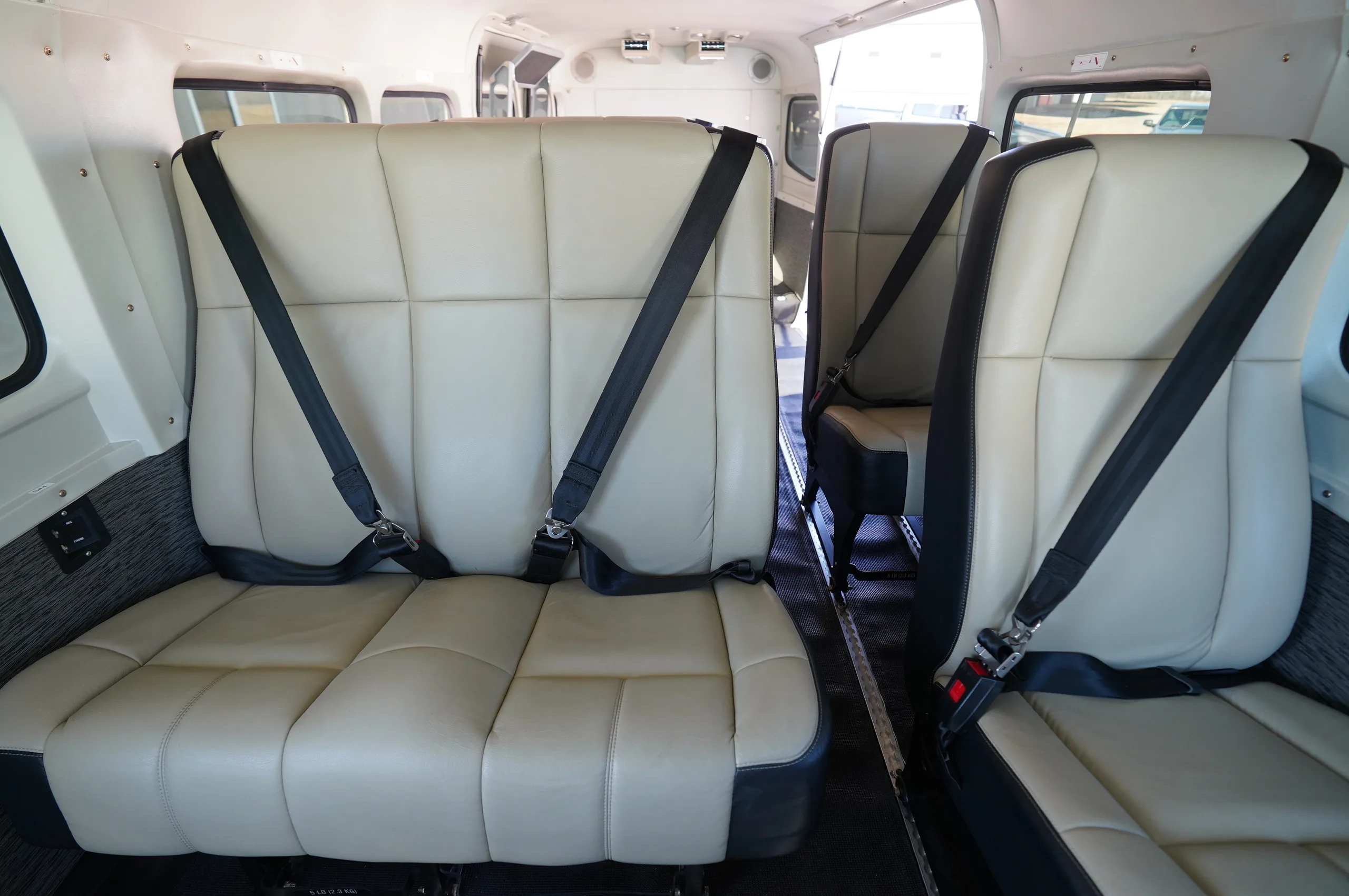 The aircraft's interior cabin with light-colored passenger seats and black seatbelts.