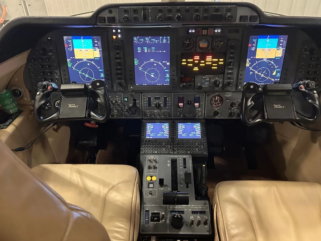 The cockpit of a Beechcraft Premier 1 jet, featuring multiple digital displays, control yokes, and a central throttle quadrant.