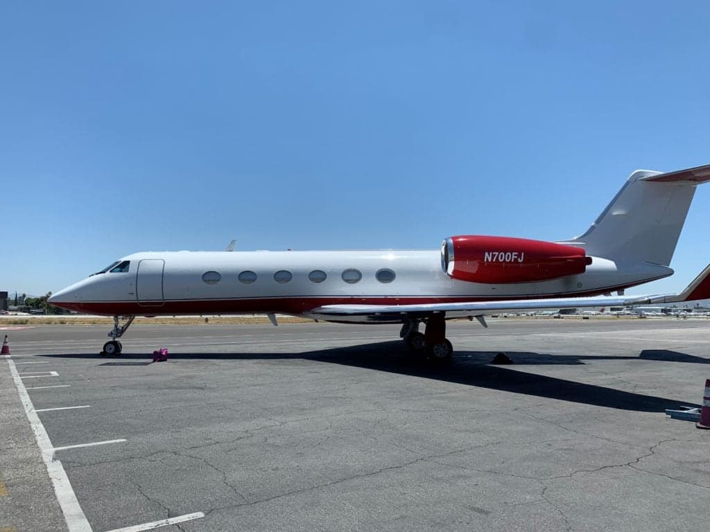 Side view of a white aircraft with red engine cowling and tail on a sunny day.