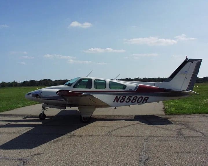 Side view of a white and maroon aircraft with tail number N8580R on a paved surface.