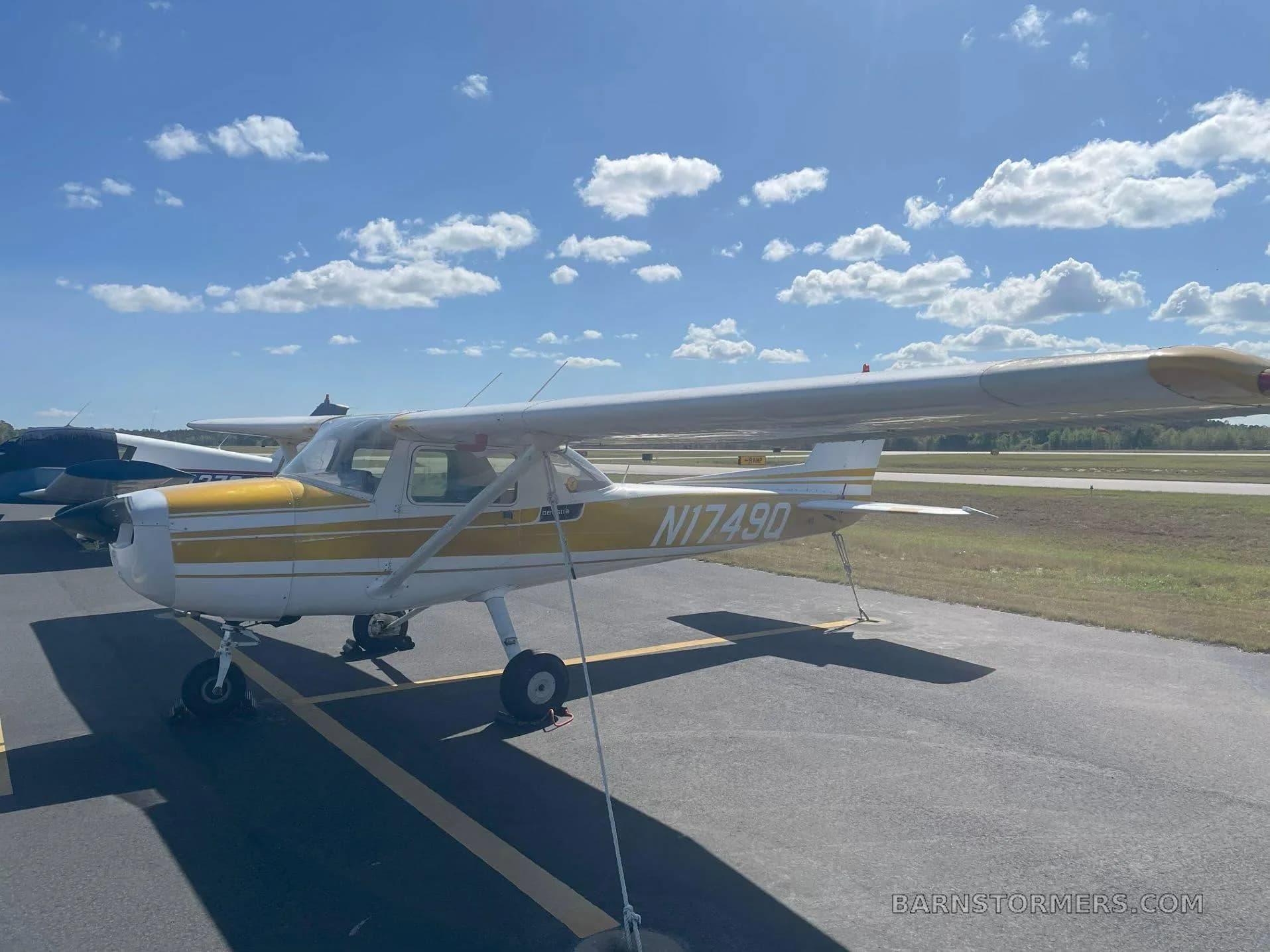 A white and yellow Cessna 172 (N1749Q) is parked on an asphalt tarmac under a blue sky with scattered clouds.