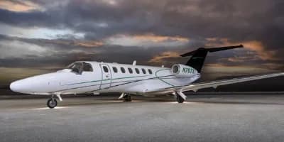 A white and green Cessna Citation CJ3 parked on a tarmac with a dramatic sky.