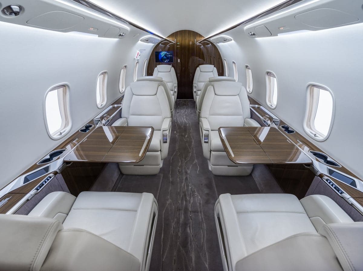 View of the aircraft's interior with white leather seats and wood tables.