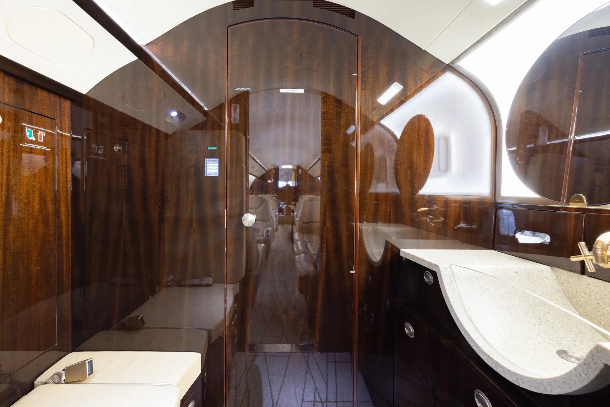 The lavatory area of a business jet with dark wood paneling, a sink, and a view into the main cabin.