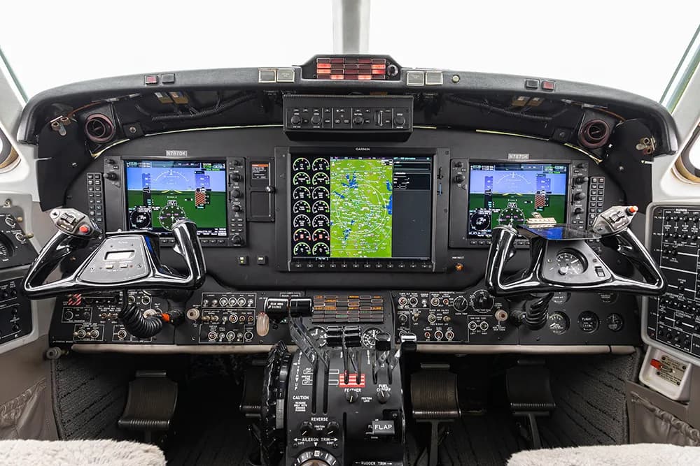 A wide-angle view of an aircraft cockpit featuring a Garmin avionics suite with multiple large screens.