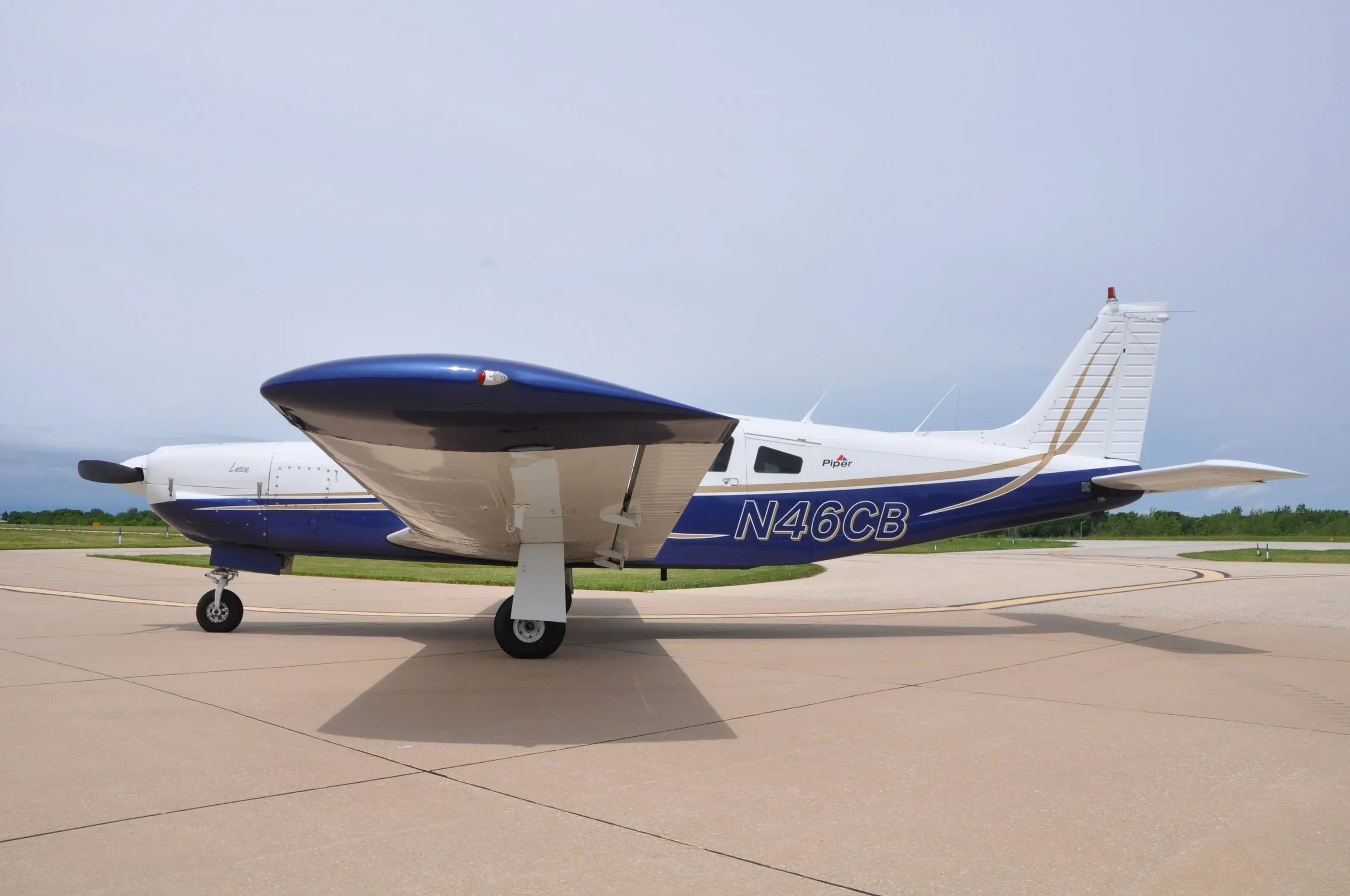 A side view of the white and blue Piper Lance aircraft (N46CB) with its landing gear visible.