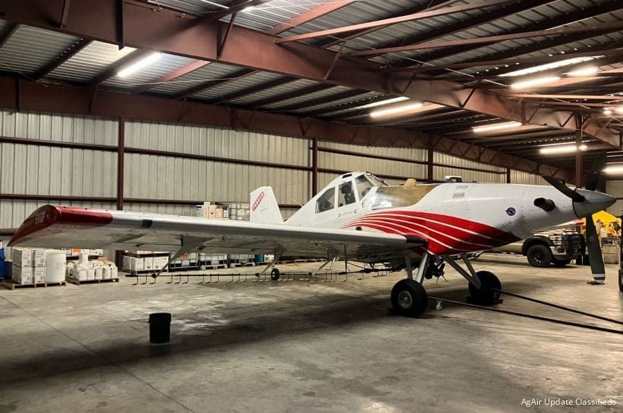 Side view of a white and red Air Tractor crop duster inside a hangar.