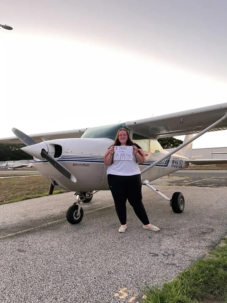 Woman standing in front of a Cessna 172 Skyhawk aircraft on the tarmac.