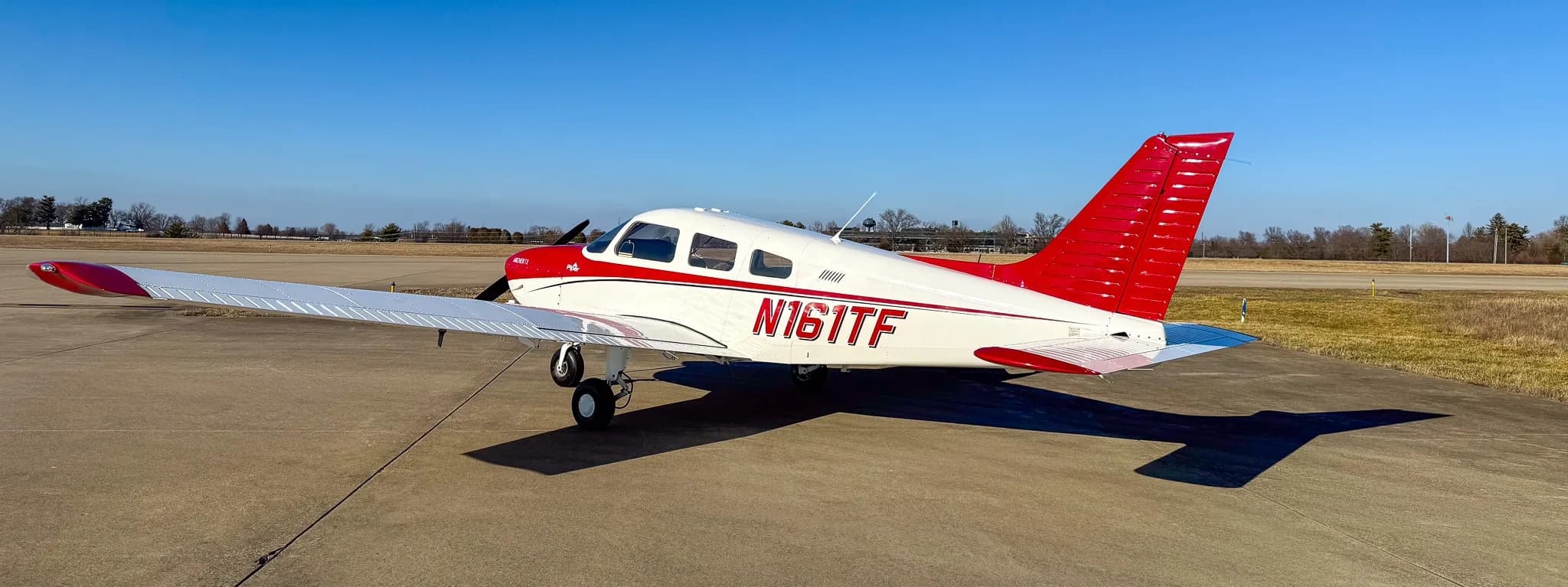 A rear-left view of a red and white Piper Archer TX aircraft, tail number N161TF, parked on an asphalt tarmac.