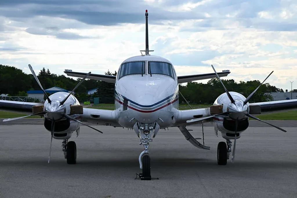 A head-on view of a white Beechcraft King Air C90GTx with blue and red stripes, parked on the tarmac.