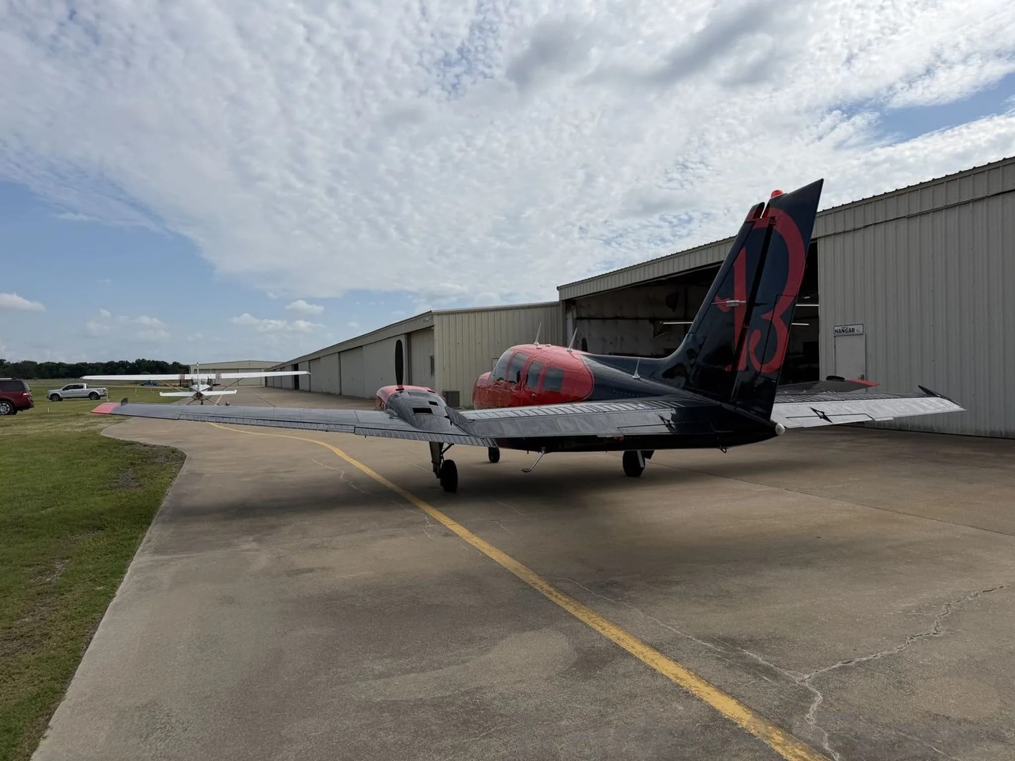 Rear three-quarter view of the red and black twin-engine propeller aircraft, N10NF, showing the red "13" on the tail, parked on an airfield.