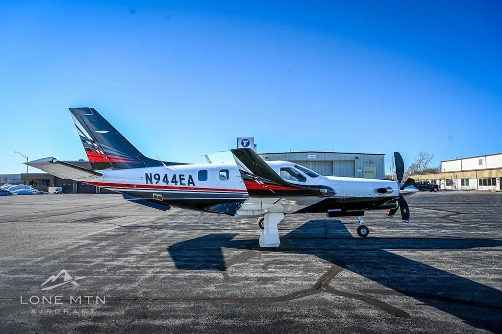 A TBM 940 aircraft, registration N944EA, parked on an asphalt ramp with a hangar in the background.