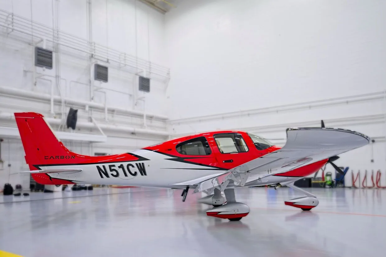 A three-quarter rear view of a red and white Cirrus SR22 aircraft with registration N51CW in a hangar.