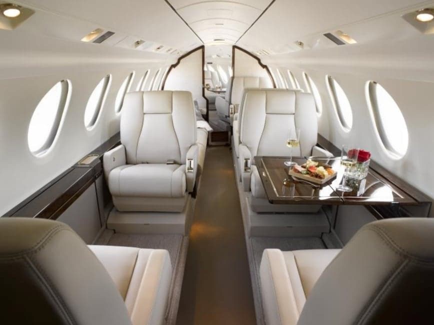 The interior of the aircraft features white leather seats and a table set for a meal.