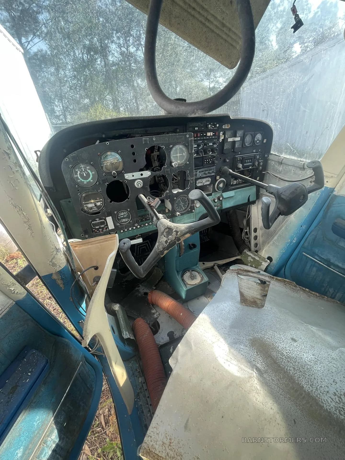 The weathered and partially stripped cockpit of a light aircraft, showing the instrument panel with missing gauges and dual yokes.