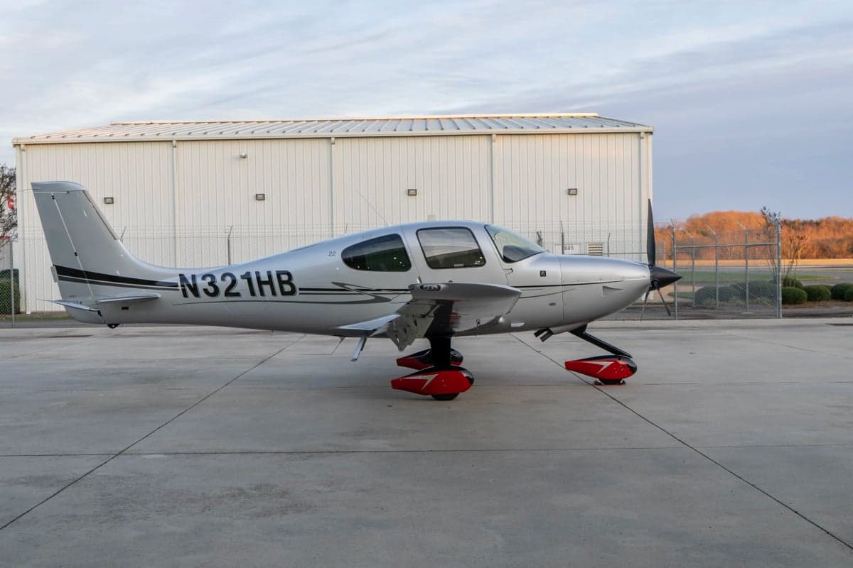 A Cirrus SR22T aircraft with a silver paint scheme parked on the tarmac.