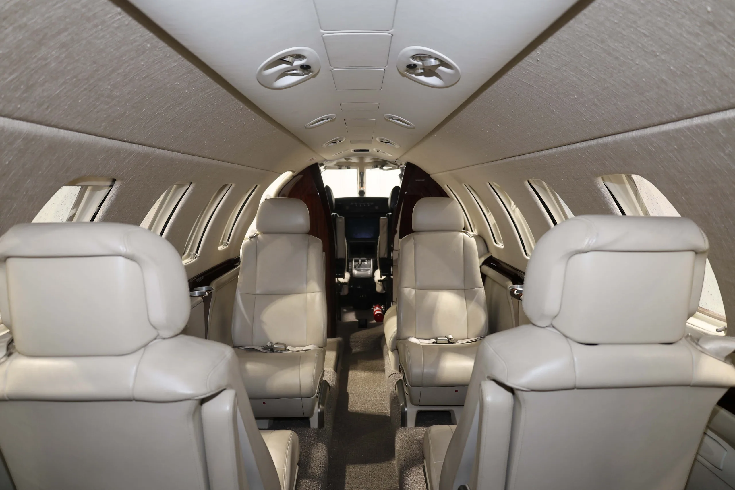 The interior cabin of a business jet with light beige leather seats facing forward and aft, looking towards the cockpit.