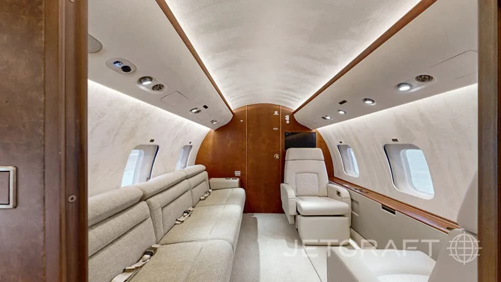 The luxurious cabin interior of a business jet, featuring a long sofa and a single cream-colored armchair.