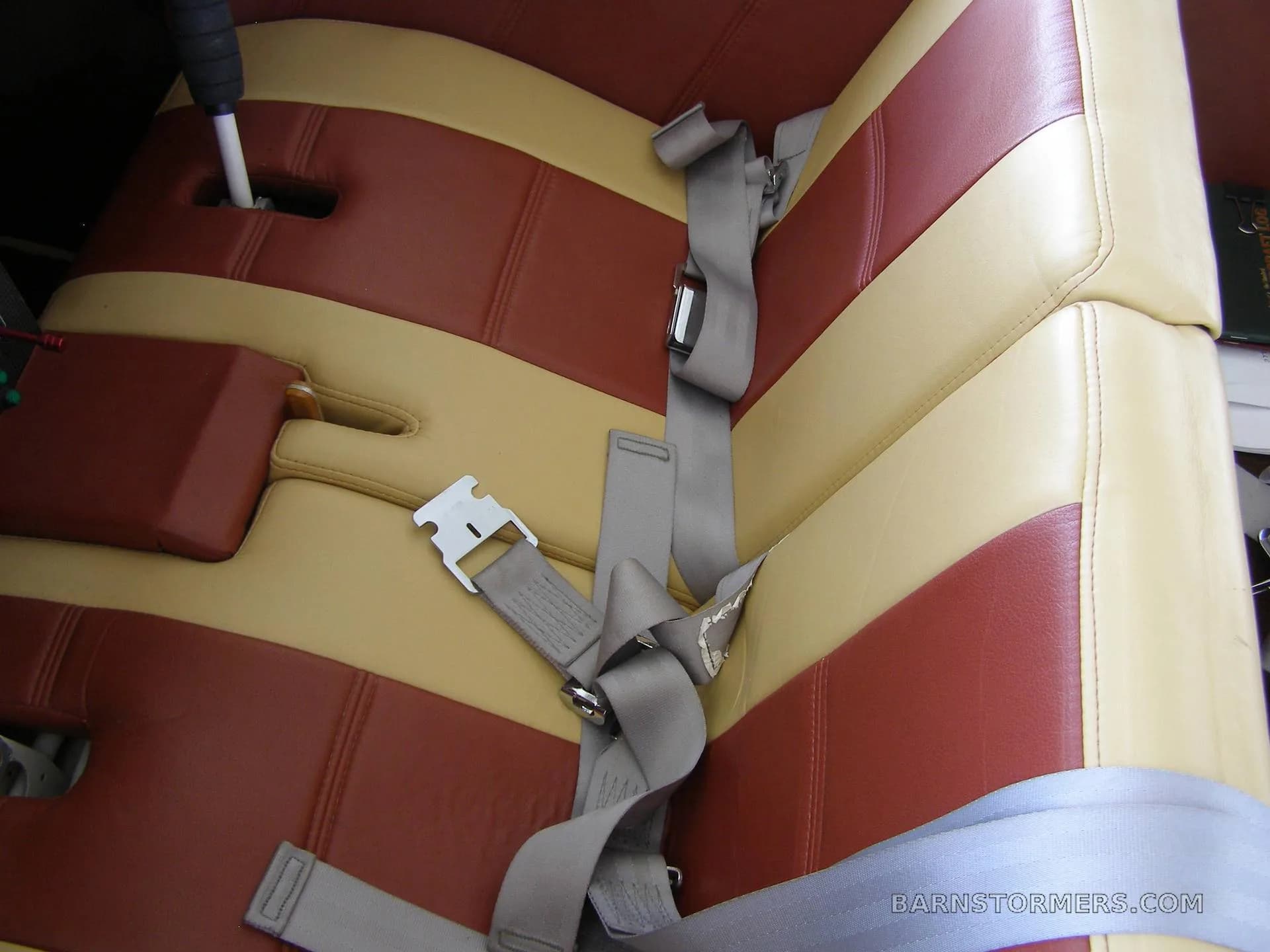 Close-up of the aircraft's interior seats, upholstered in red and tan stripes, with gray seatbelts.