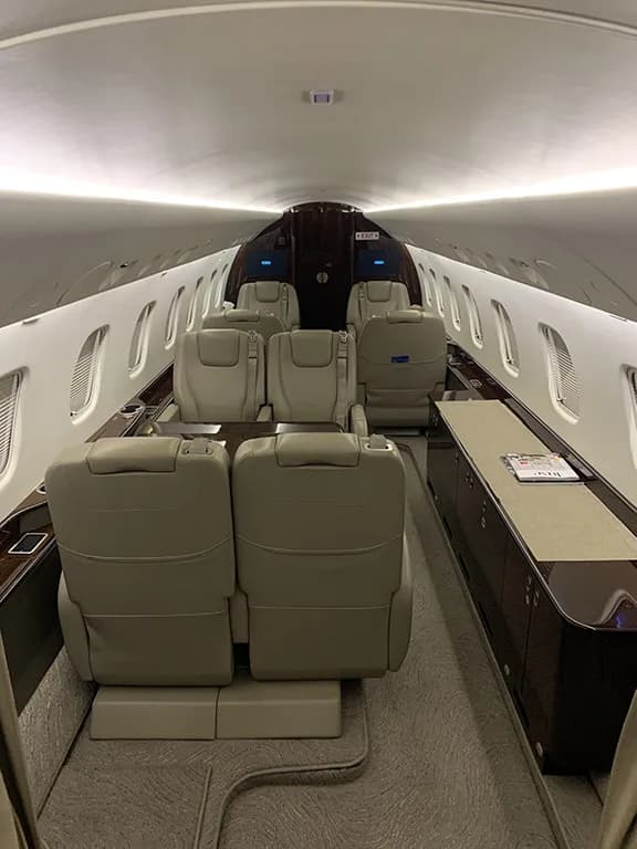 A long view down the aisle of the Embraer Legacy 650's private jet cabin with multiple rows of beige seats.