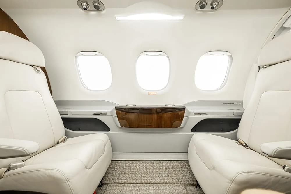 Two cream leather passenger seats facing each other in the Embraer Phenom 100E cabin, with a small wooden table between them.
