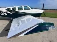 A Beechcraft Bonanza with a white and green paint scheme is parked on the tarmac.
