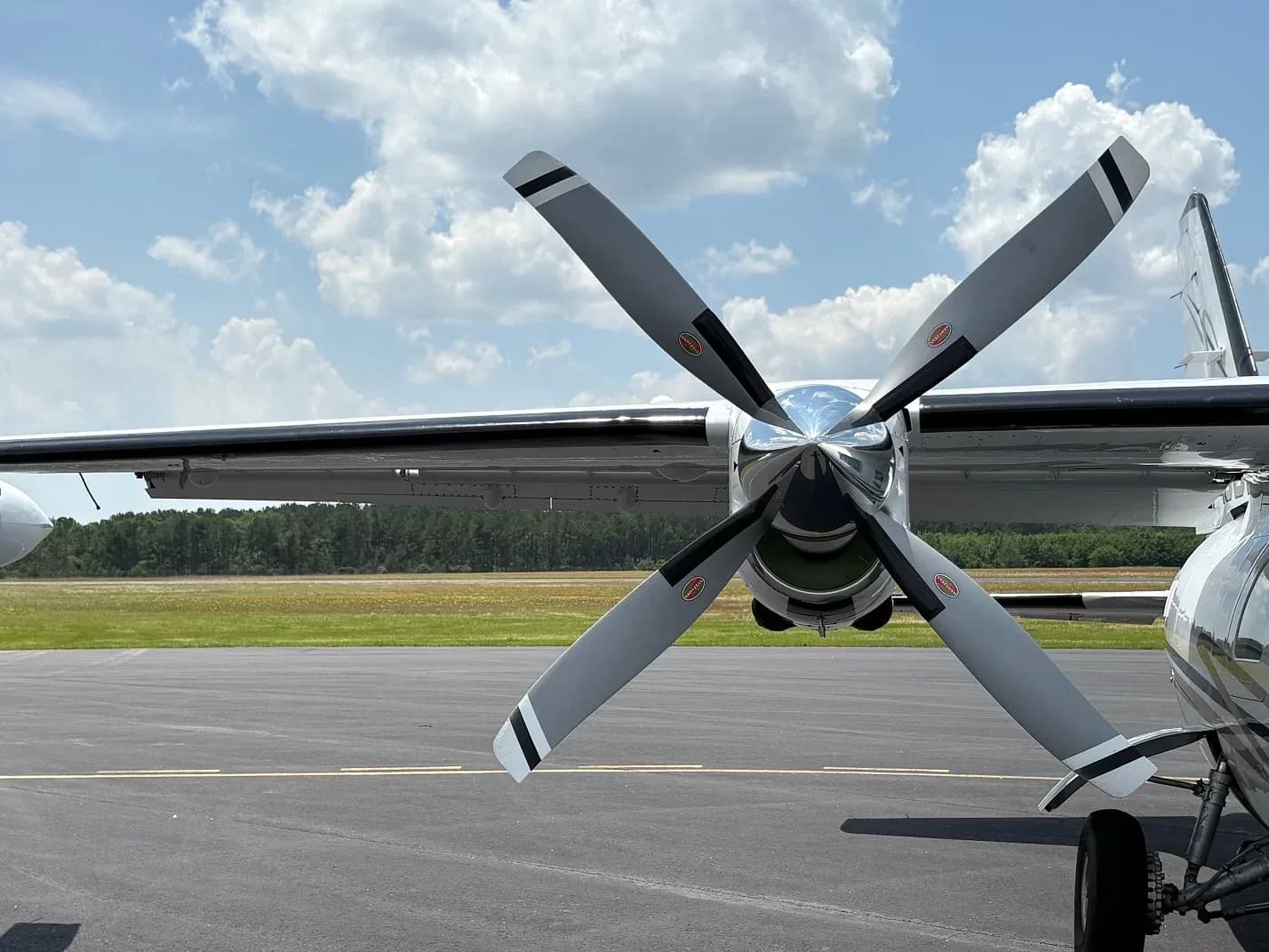 Close-up of the four-blade propeller and engine nacelle of a white aircraft on an airfield.