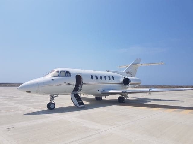Side view of a white jet aircraft with the door and stairs open on the tarmac.
