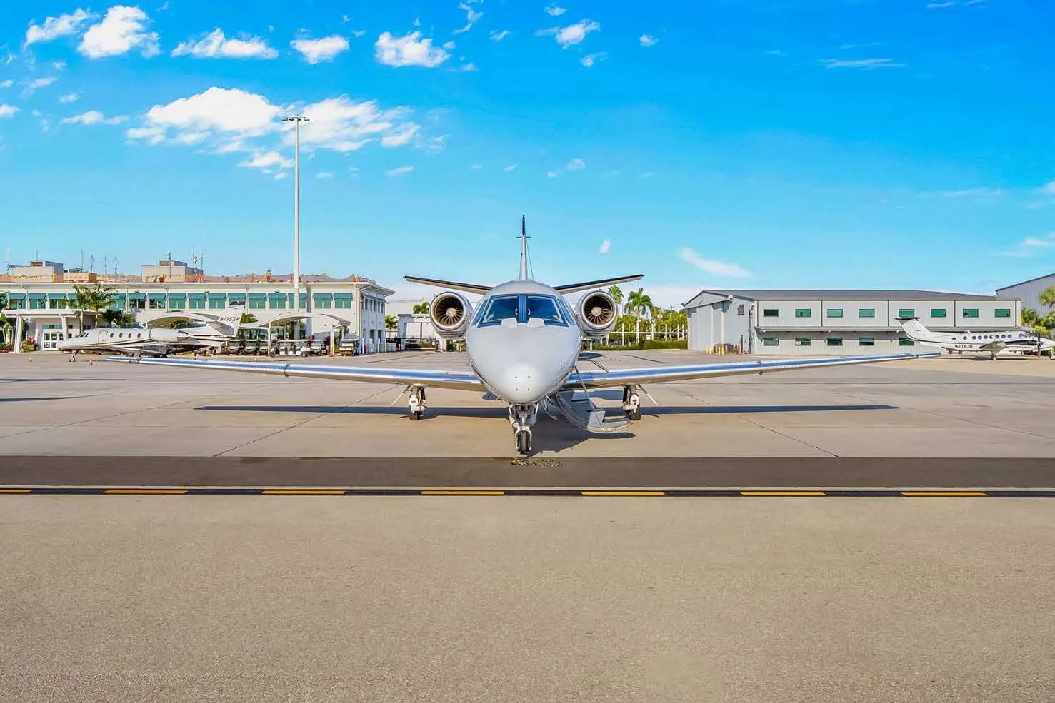 A head-on view of a white Cessna Citation business jet, N846JS, parked on an airport tarmac with hangars and other aircraft in the background.