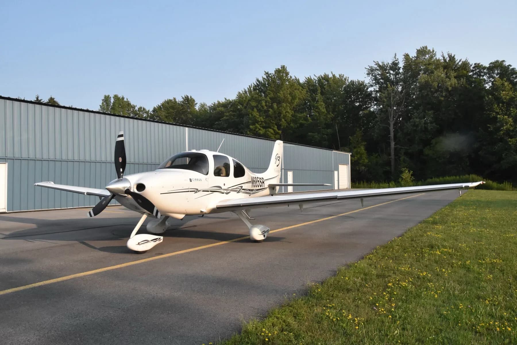 A front-quarter view of the white Cirrus SR22T aircraft (N685SR) parked in front of a hangar.