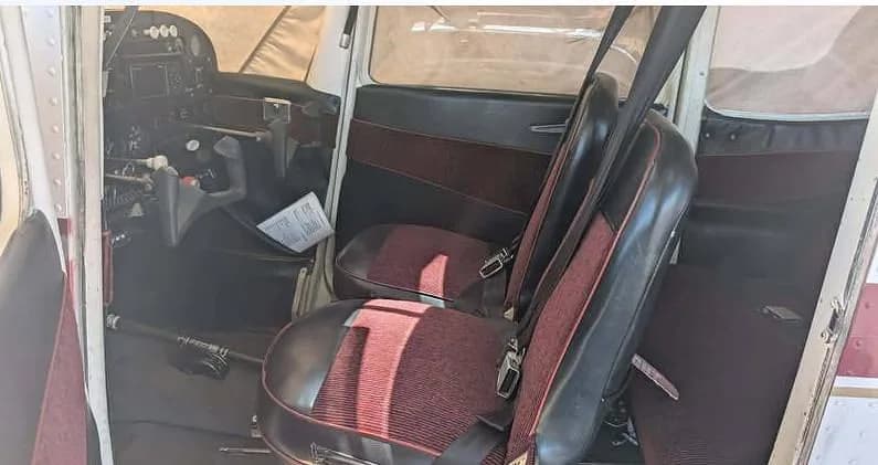 An interior view of the Cessna 172M cabin, showing the front seats with maroon striped fabric and a partial view of the instrument panel.