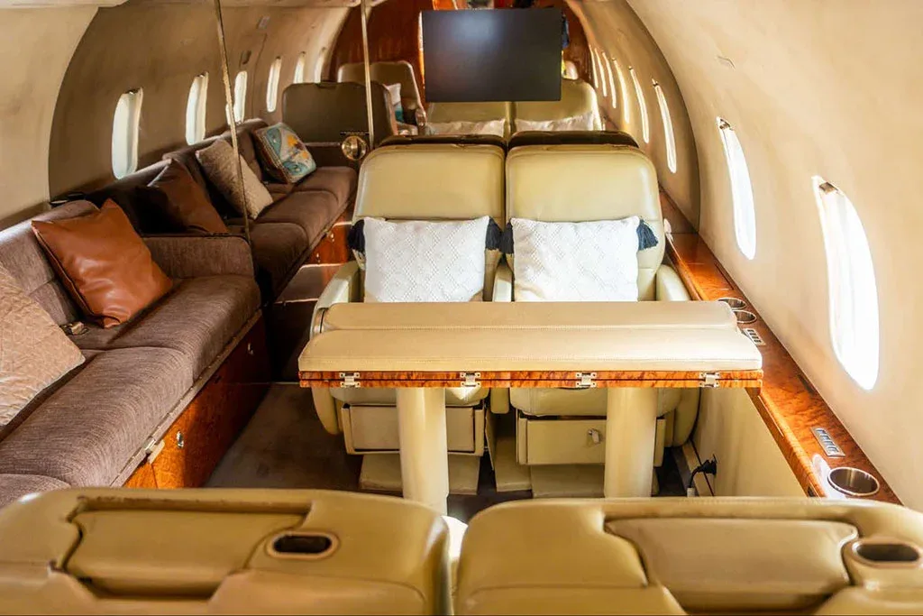 A wide view of a private jet cabin interior with a dining table, facing seats, and a long sofa.