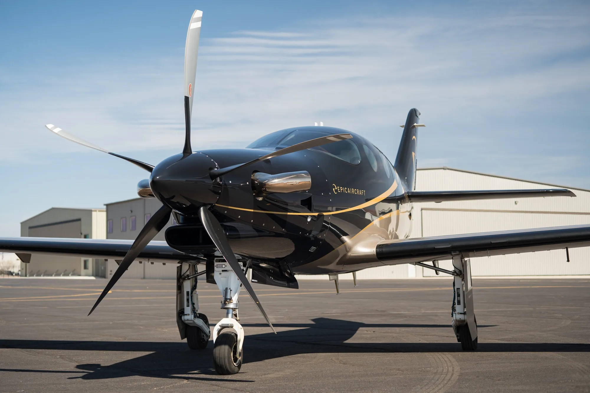 A close-up front view of the black and gold Epic E1000 GX aircraft on the tarmac.