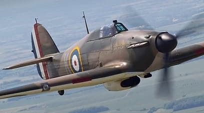 Hawker Hurricane fighter in flight over the ocean near a lighthouse.