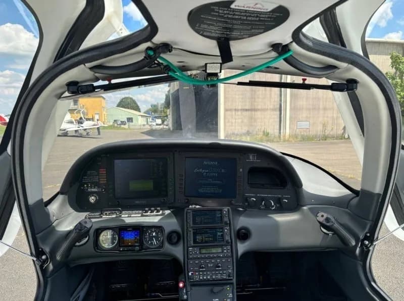 Cockpit view from the pilot's seat showing the instrument panel and an airfield through the windshield.