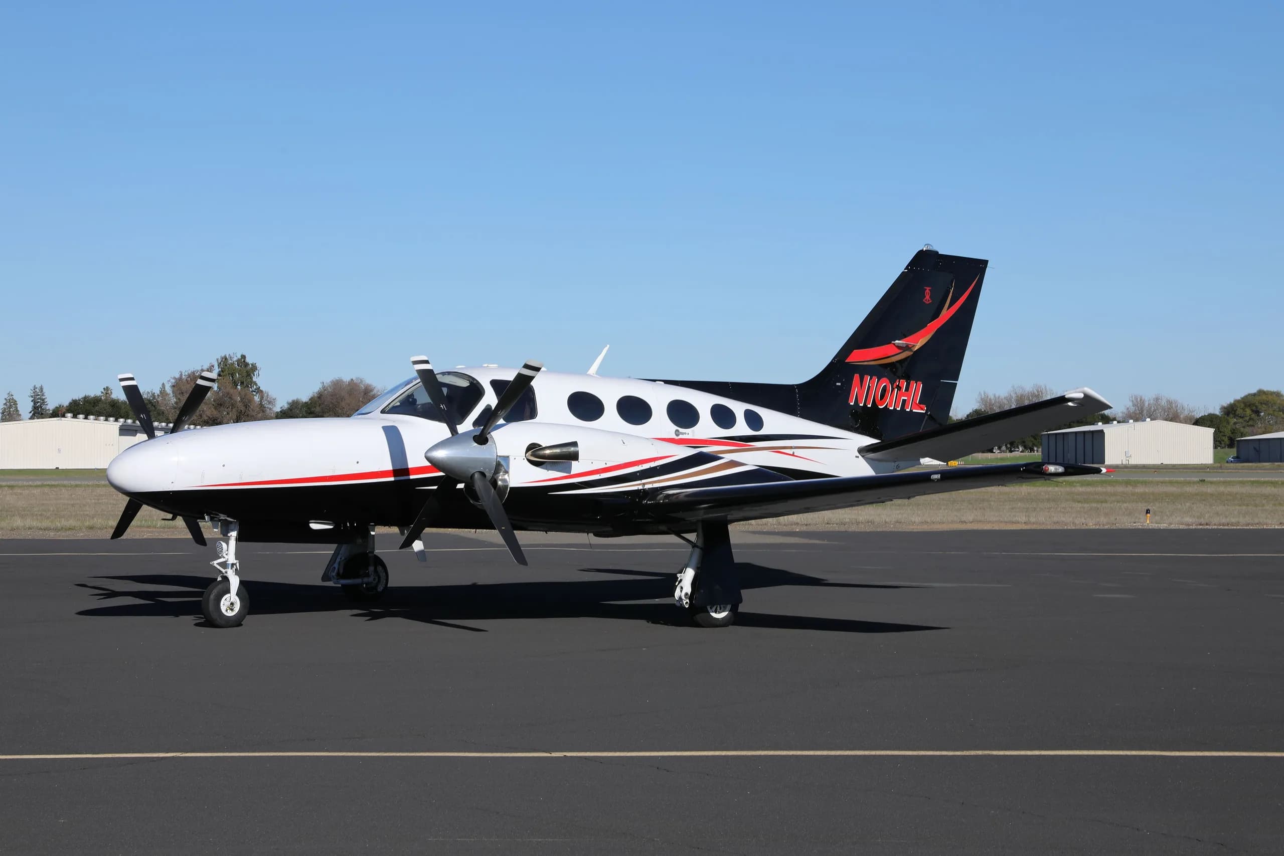 A white, black, and red Cessna 414 Chancellor parked on an asphalt tarmac under a clear sky.