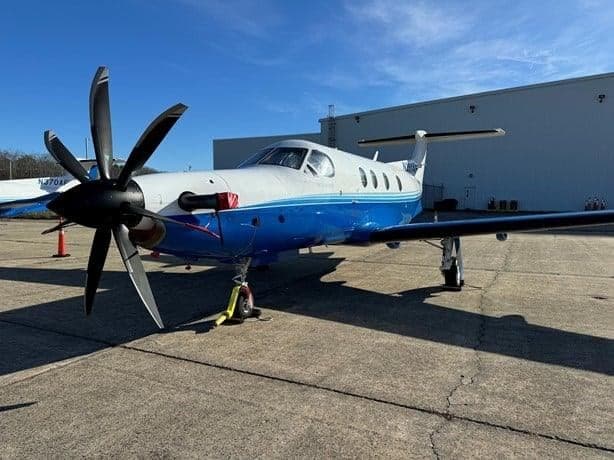 A blue and white Pilatus PC-12 aircraft is parked on the tarmac.