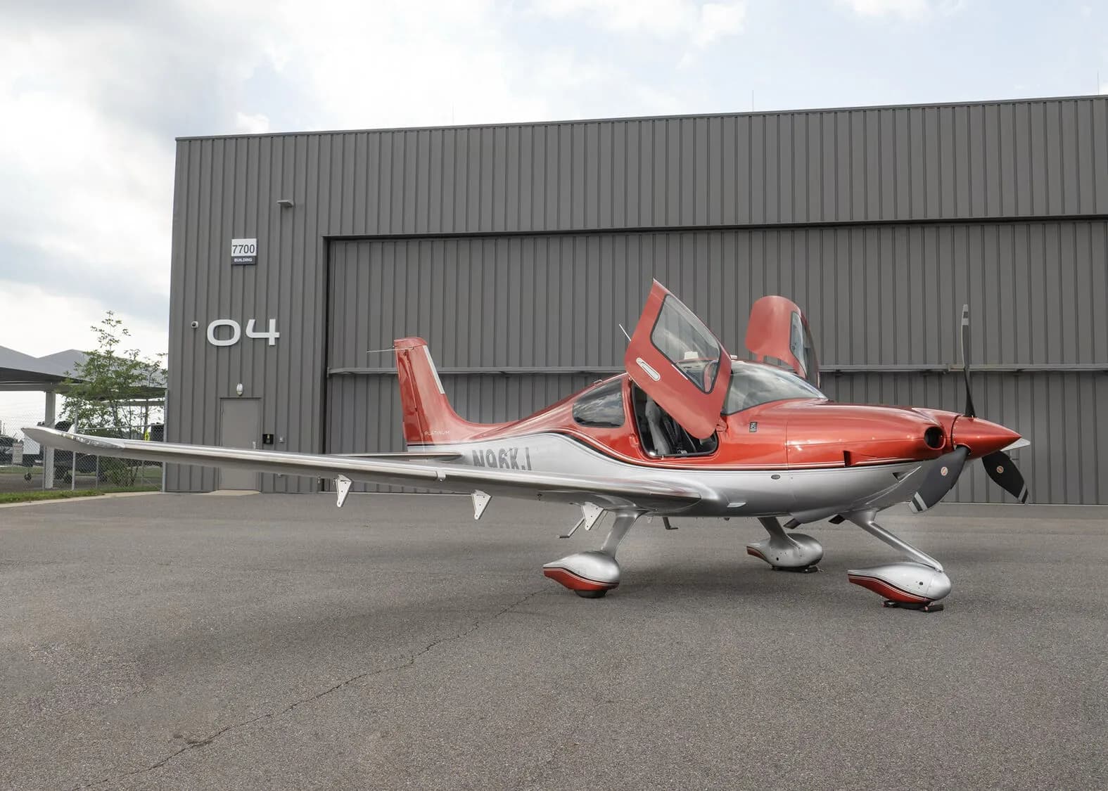 A three-quarter front view of a red and silver Cirrus SR22T aircraft, registration N96KJ, with its gull-wing doors open.