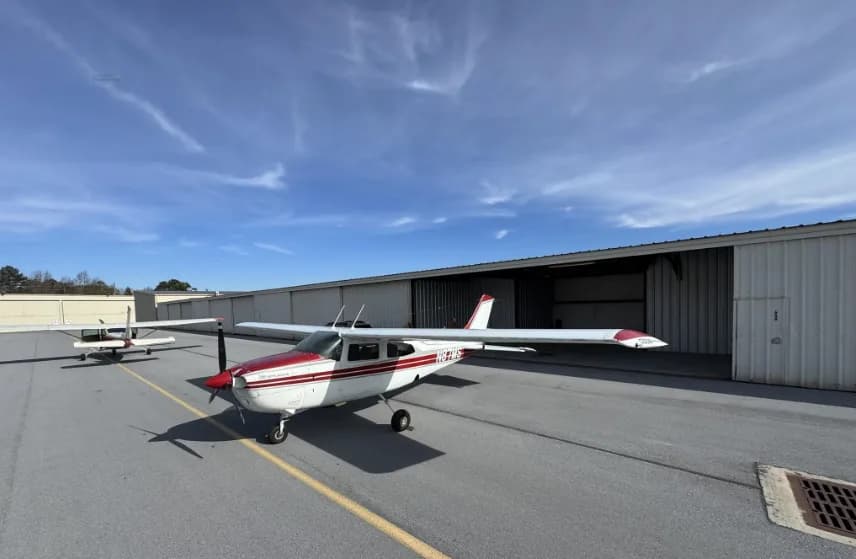 A white and red Cessna 182 Skylane (N87MS) parked on an airport tarmac with hangars in the background.