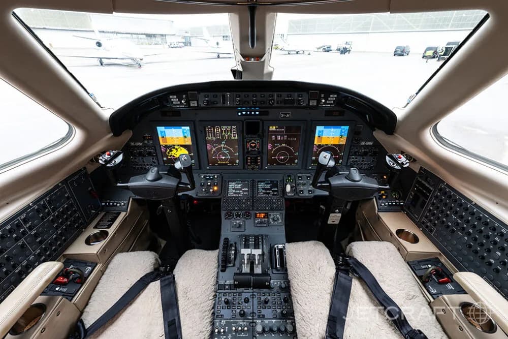The spacious cockpit of a business jet with multiple digital displays and light-colored sheepskin seat covers.