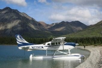 A white and blue Cessna 206 on floats speeds across the water.