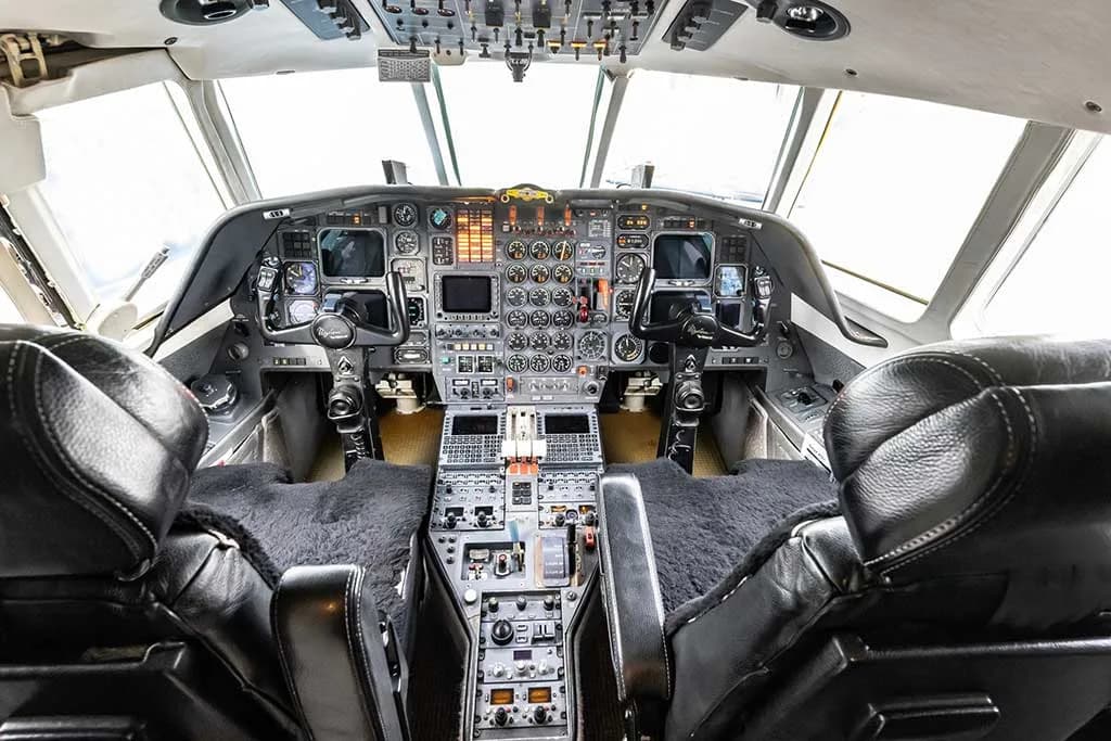 The cockpit of a Dassault Falcon 900EX, showing the instrument panel, controls, and two pilot seats with sheepskin covers.